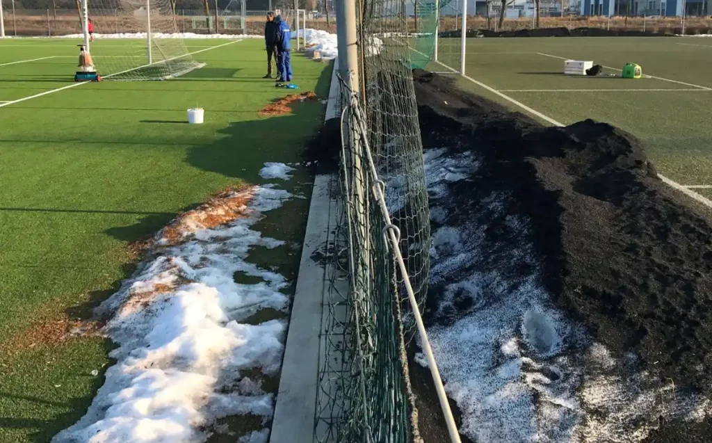 Snow on two playing fields with two men chatting in the distance.