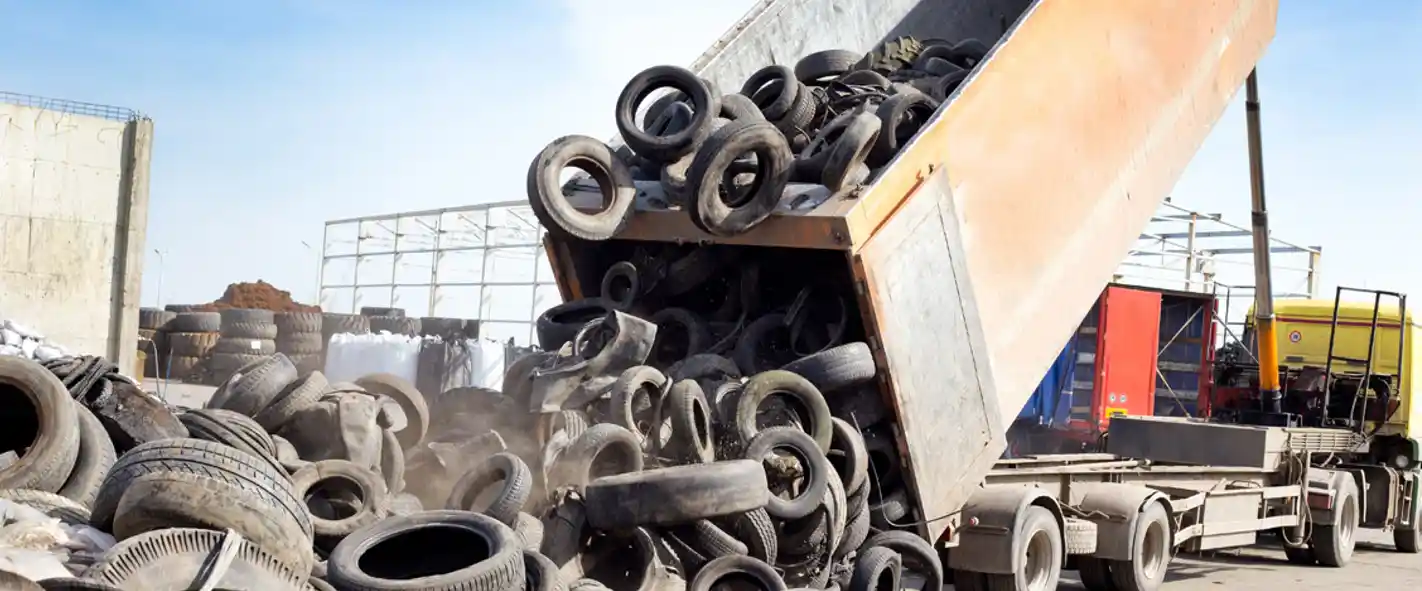 A trucks dumps out old tyres onto the ground.